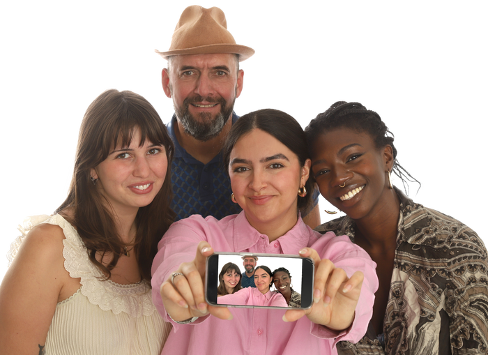 Vier Personen, die vordere Person hält ein Handy, welches ein Selbstporträt auf dem Display anzeigt